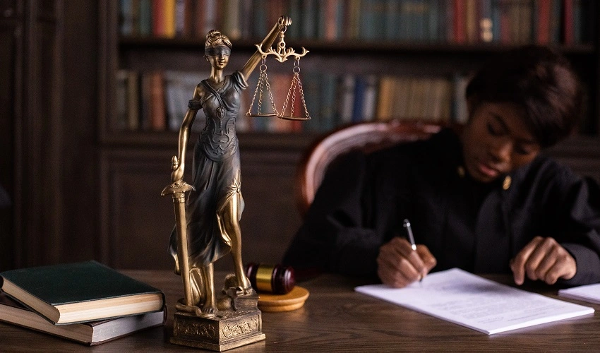 Lady justice statue on a desk with a person writing on a document