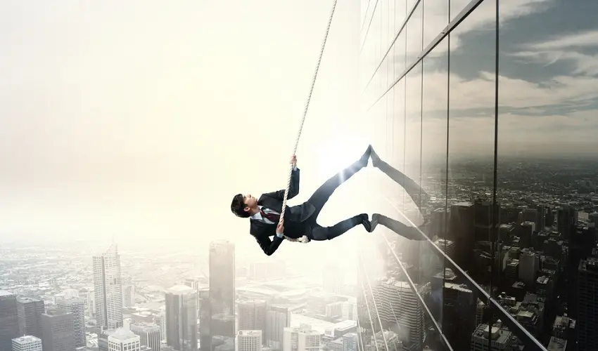 Determined businessman climbing building with help of rope