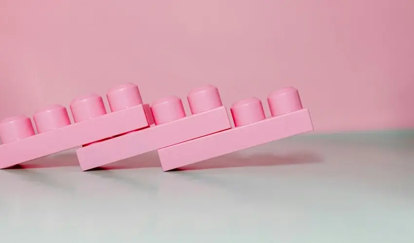 Three pink plastic toy bricks leaning diagonally against each other on a pink background.