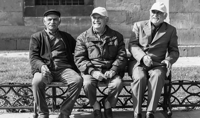 Three old men sitting on bench smiling in black and white